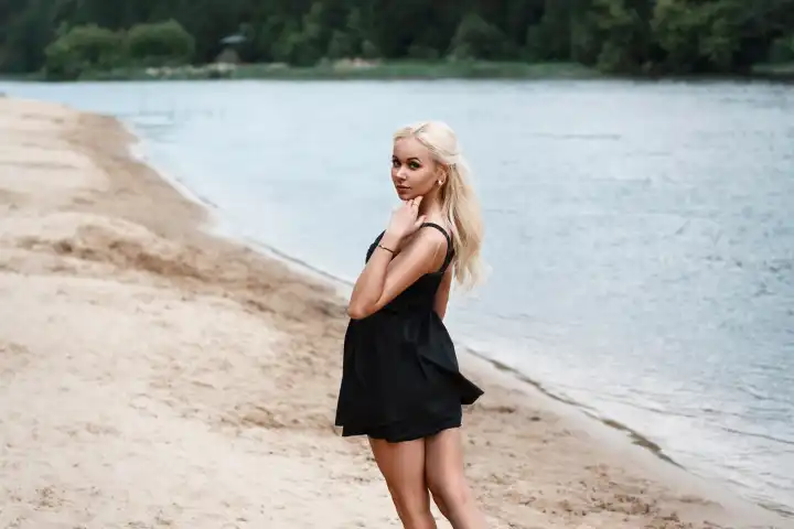 Schöne Frau Schöne weibliche Beine gehen in das Wasser stehend in schwarzem Kleid am Strand