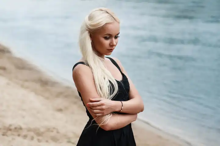 Hübsche Frau im schwarzen Kleid am Strand