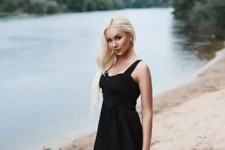 Porträt einer schönen Frau in einem schwarzen Kleid am Strand am Fluss