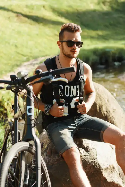 Stilvoller junger Mann mit einem Fahrrad auf einem Felsen sitzend. Schwarzes T-Shirt mit Aufdruck 23