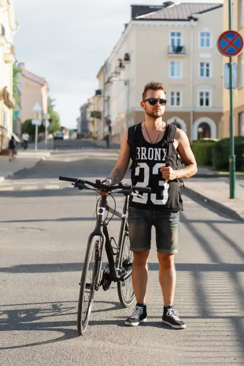 Junger Hipster Mann mit Fahrrad zu Fuß in der Stadt. Schwarzes T-Shirt mit Druck 23