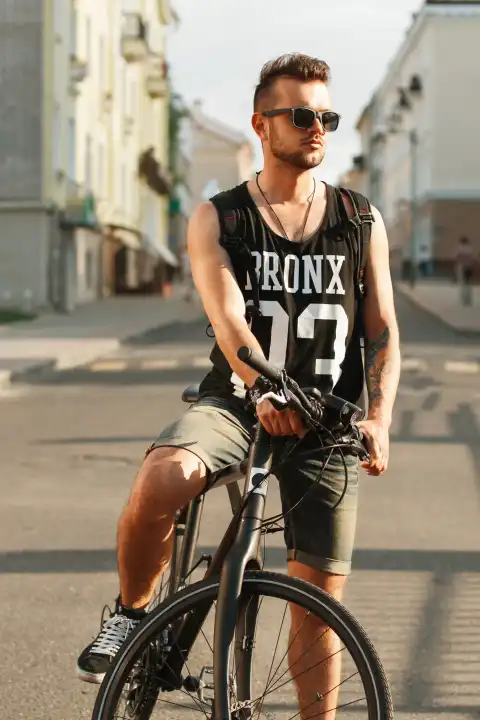 Junger Hipster Mann mit Fahrrad sitzt auf einem Fahrrad in der Stadt. Schwarzes T-Shirt mit Druck 23