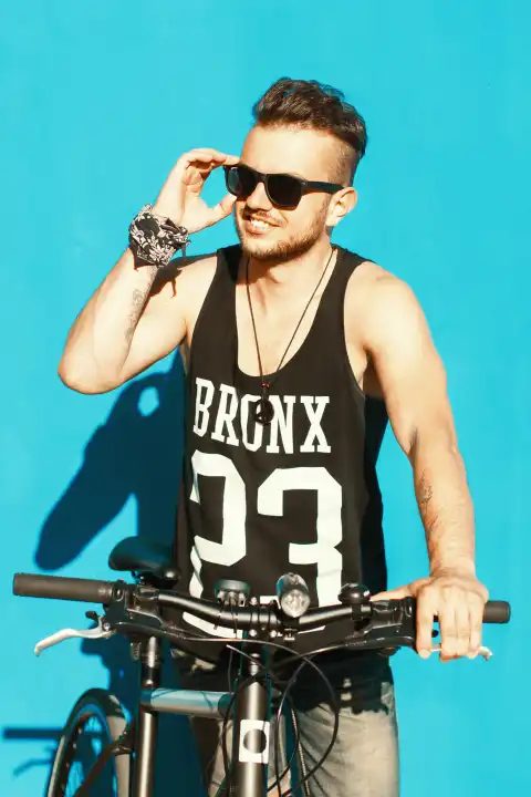 Hipster mit einem Fahrrad in der Nähe einer hellblauen Wand.