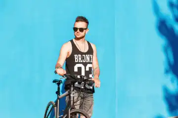 Hipster man with sunglasses with a bike near a bright blue wall.