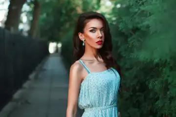 Beautiful fashion woman walking in the park in a turquoise dress.