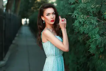 Beautiful girl in a dress with earrings near the green bush.