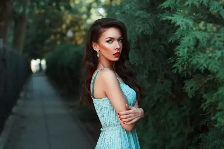 Modeporträt einer hübschen Frau in einem türkisfarbenen Kleid im Park.