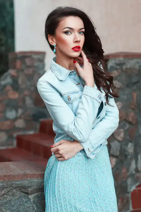 Schöne hübsche Frau in einer Jeansjacke und türkisfarbenem Kleid in der Nähe von Stein