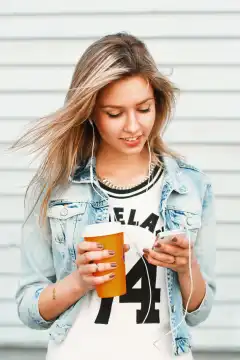 Beautiful happy hipster girl listens to music on the phone and drinking coffee.