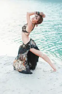 Beautiful girl dancing in tribal style on white sand beach near the water