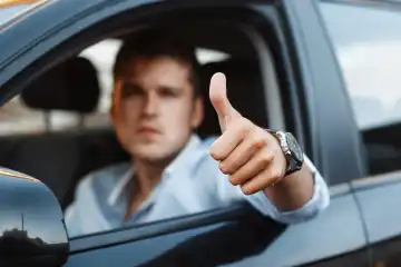 Handsome man sitting in a car and holding thumbs up