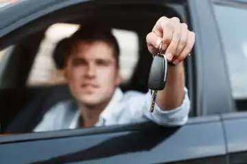 Businessman sitting in a car and giving a car key.