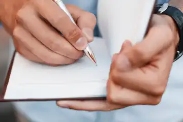 Man writing notes in a notebook. Hand holding pen