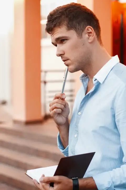Junger Mann mit Notizbuch und Stift, der über seine Arbeit nachdenkt.