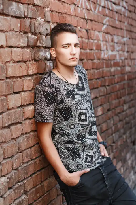 Junger Hipster in schwarzem Hemd steht in der Nähe einer roten Backsteinmauer mit Graffiti.