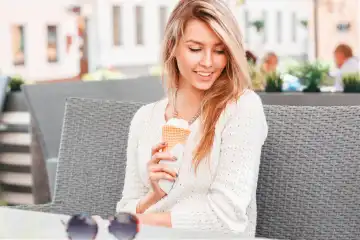 Beautiful girl sitting in a summer cafe and eating ice cream in a waffle cone. Woman hand holding waffle with ice cream.