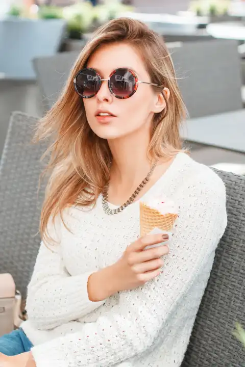 Modisches schönes Mädchen mit runder Sonnenbrille und Eis in einem Sommercafé sitzend.