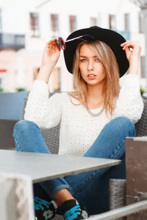 Porträt einer jungen hübschen Frau mit einem schwarzen Hut und einer runden Sonnenbrille. Schönes Mädchen sitzt im Sommercafé.