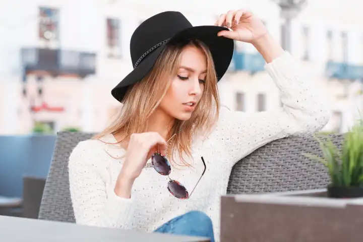 Schönes stilvolles Mädchen mit Hut und Sonnenbrille ruht sich an einem sonnigen Tag in einem Café aus