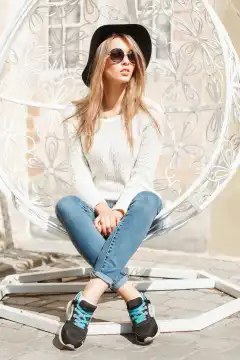 Beautiful fashionable girl sitting in a white suspended chair.