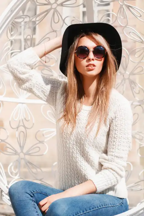 Hübsche Frau mit Hut und Sonnenbrille ruht sich an einem sonnigen Tag in einem weißen Hängesessel aus