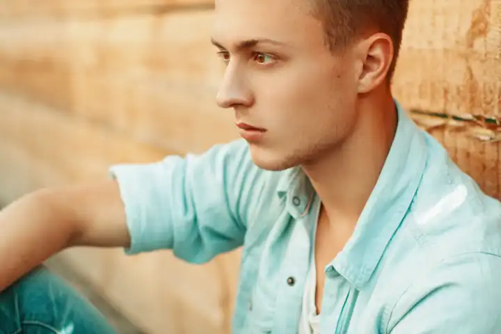 Young sad man in denim clothes on the background of wooden wall