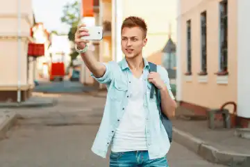 Moderne touristYoung Junge in der Nähe einer Holzwand tun ein Selbstporträt auf dem Telefon auf dem Hintergrund der Stadt