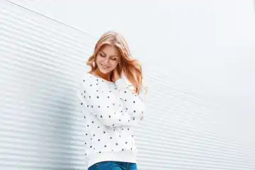Fashion portrait of beautiful young blond hair women in a white sweater and jeans against a white wall.