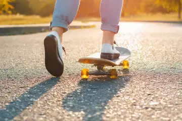 Frau auf dem Skateboard bei Sonnenaufgang. Beine auf dem Skateboard, bewegt sich zum Erfolg