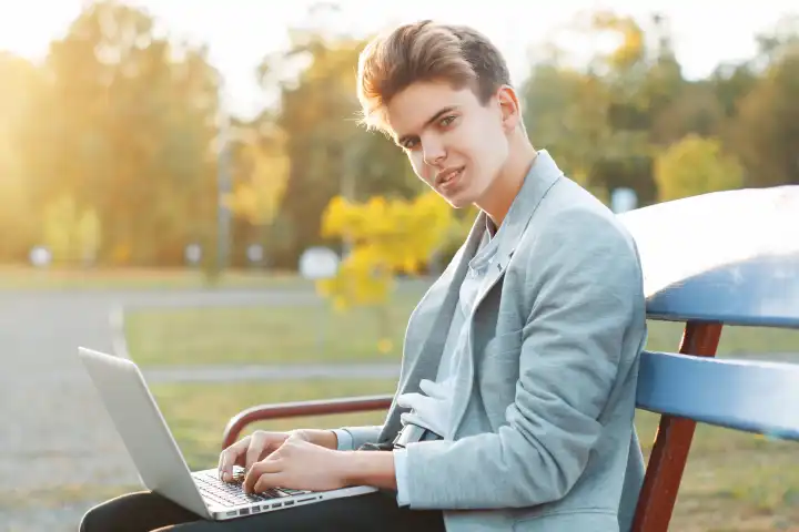 Junger gut aussehender Mann sitzt bei Sonnenuntergang auf einer Bank im Park. Hält ein Notizbuch in den Händen und arbeitet.