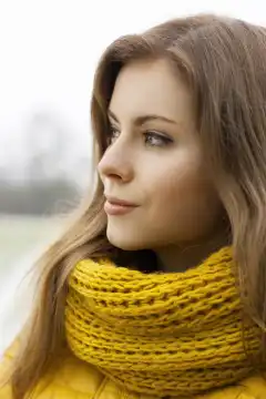 Pretty woman in a yellow knit scarf looks into the distance. Outdoor portrait.