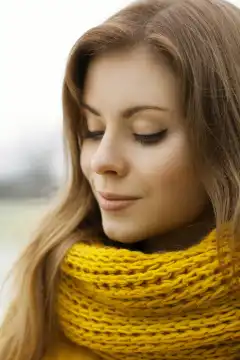 Pretty woman in a yellow knit scarf with eyes closed. Outdoor portrait.