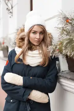 Beautiful girl in a knitted hat and jacket standing near the wall with Christmas decorations.