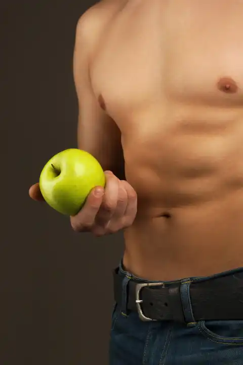 Mann hält den Apfel. Bauchmuskeln und Brust. Sportler im Studio.