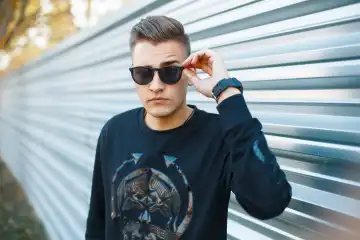 Young handsome man in sunglasses in the autumn sunny day on the background wall of metal