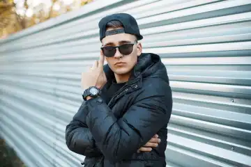 A young man in a stylish winter jacket and sunglasses on the background of a metal wall.