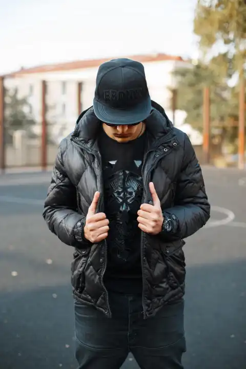 Junger, trendiger Mann mit schwarzer Mütze und schwarzer Jacke auf der Straße