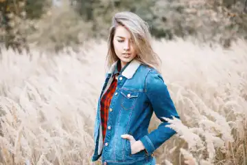 Junges Mädchen in Jeanskleidung und rot kariertem Hemd im Herbstfeld mit Gras