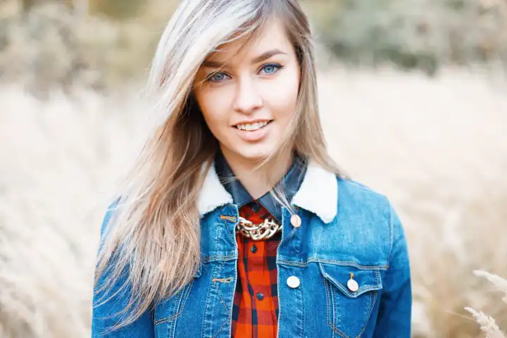 Porträt eines schönen Mädchens in Jeanskleid auf einem Hintergrund von Herbstgras