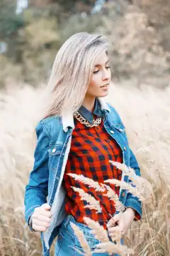 Fashionable stylish girl in a denim dress and a red checkered shirt in the autumn field with grass