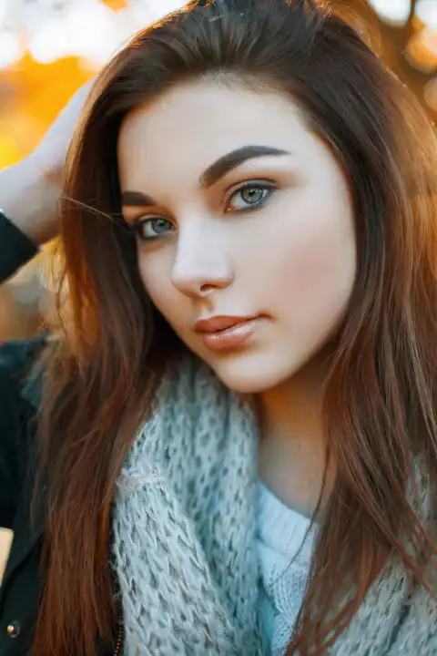 Close-up portrait of a beautiful young girl in a gray knitted scarf on the background of autumn park