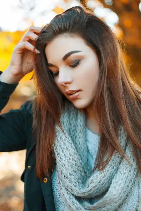 Close-up portrait of a young beautiful girl in knitted sweater, scarf and a black jacket in the autumn park