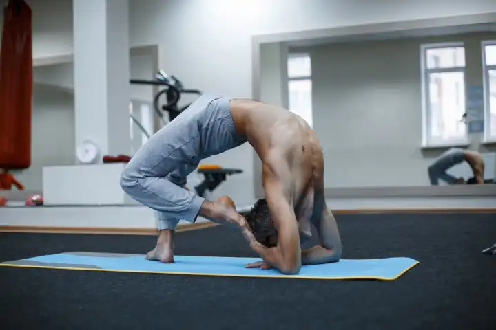 Athletic muscular young man working out, yoga, pilates, fitness training, doing side bend, asana Parighasana, Gate Yoga Pose in gym