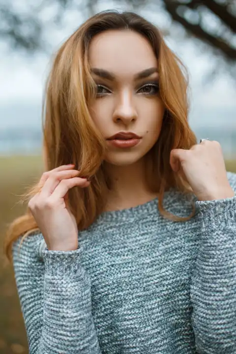 Close-up portrait of a beautiful young girl in stylish winter sweater on the background of a tree with fog