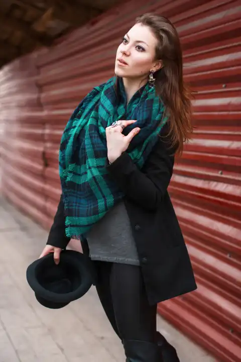Portrait of a beautiful girl in a coat with a scarf. Hat in hand.