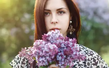 Spring portrait of a pretty woman holding a lilac flowers. Outdoors portrait.
