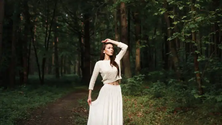 Hübsche Frau im weißen Kleid erkundet einen schönen Wald.