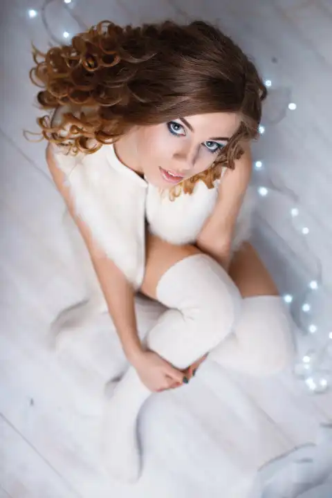Young beautiful girl in a warm vest and knitted socks sitting on the floor against a background of lights. Top view