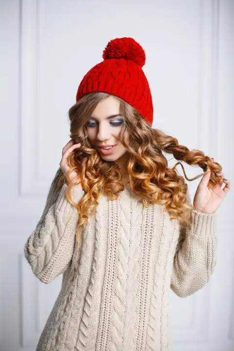 Young girl with curly hair in a red knitted hat and a warm sweater