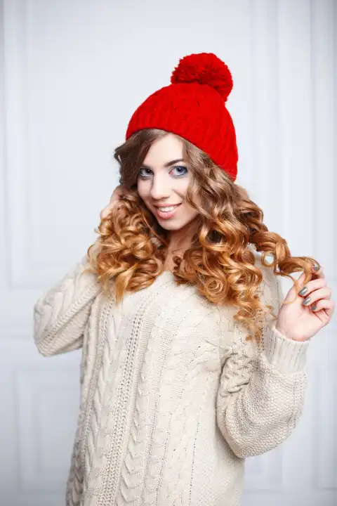 Fashionable young girl with curly hair in a red knitted hat and vintage sweater.